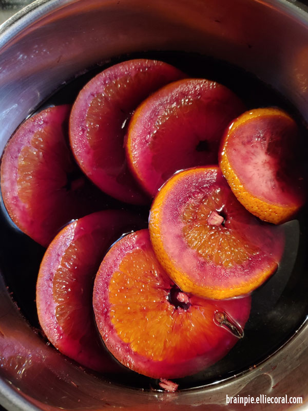 A pot of orange slices tinged red from wine.