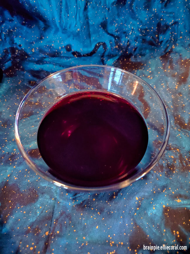 A clear glass of dark red wine.