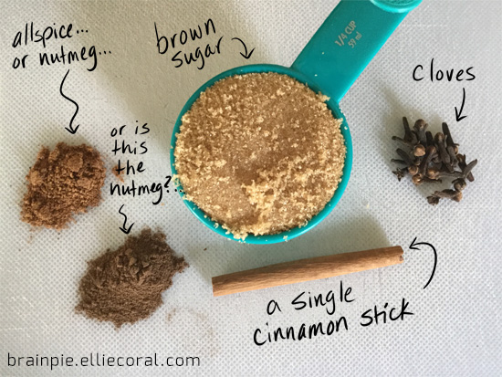 A spread of ingredients including allspice or nutmeg... or maybe the other pile is nutmeg... a cup of brown sugar, a single cinnamon stick, and some whole cloves.