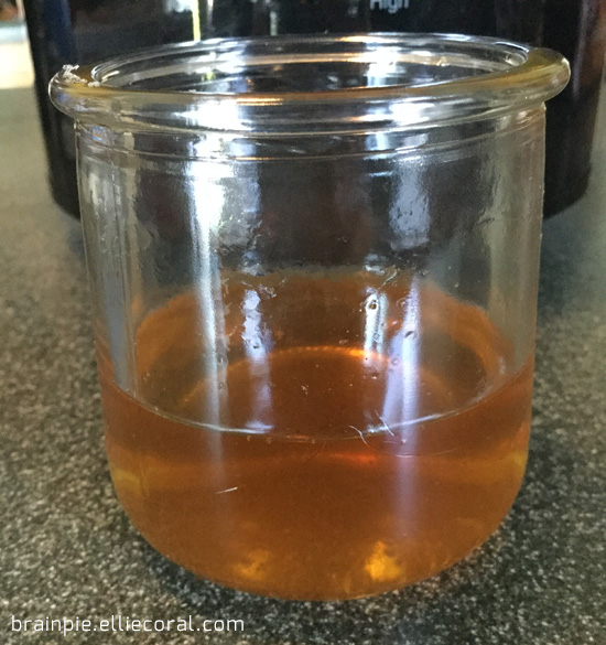 A glass yogurt container holds one-quarter of amber cider.