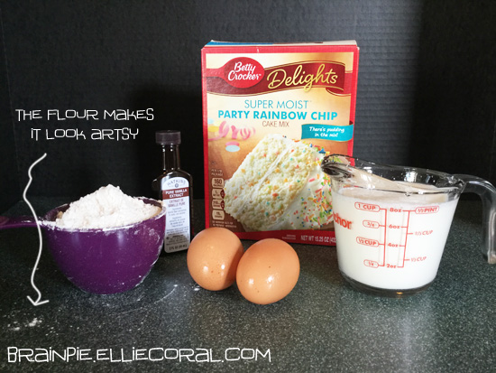 An arrangement of ingredients including a cup of flour, pure vanilla extract, two brown eggs, a box of Betty Crocker super moist party rainbow chip cake mix, and a glass measuring cup of milk. The flour speckled around the counter makes the setup look artsy.