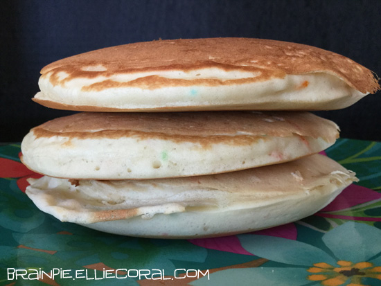 Three fluffy pancakes with confetti pieces sit on a plate.