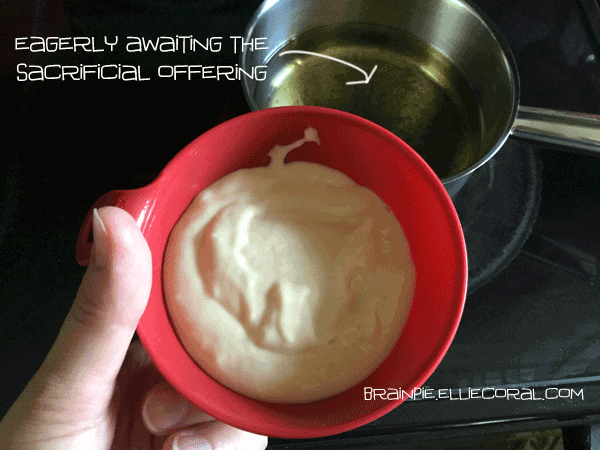 My hand with the funnel that contains the cake mix. Off to the side is a stove with the oil. The text reads: eagerly awaiting the sacrificial offering.