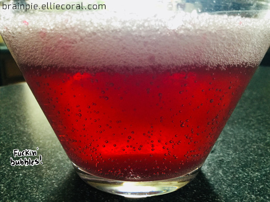 A closeup of the red liquid and pink foam, which appears more white in this photo. Bubbles rise from the bottom of the glass. Text reads, 'Fuckin' bubbles!'