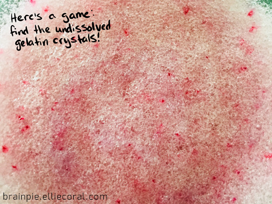 An extreme closeup of the fizz, dotted throughout with red crystals. Text reads, 'Here's a game: find the undissolved gelatin crystals!'