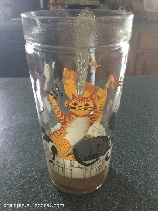 A clear glass decorated with alley cats sitting on a white fence.