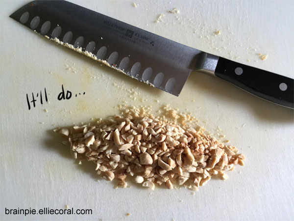 A cutting board with a small pile of chopped peanuts with a peanut-encrusted knife sitting nearby.