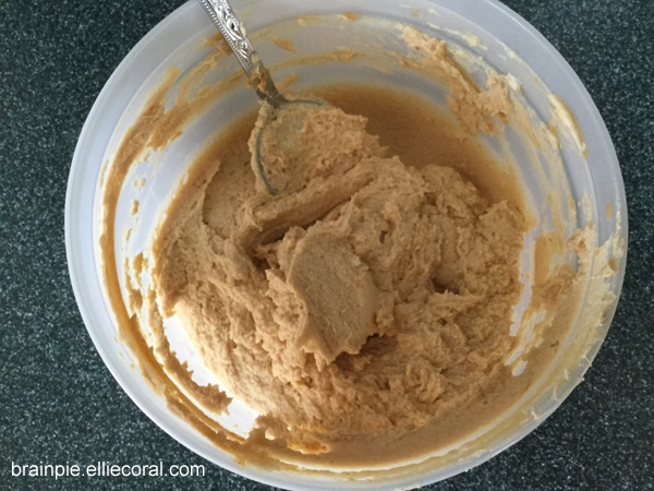 Another plastic bowl with peanut butter, hot sauce, cream cheese, and Worcestershire sauce mixed into a lovely beige paste. A spoon sits on the side of the mixture.