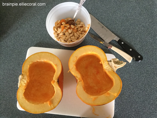 The guts have been scooped out of the pie pumpkin halves, leaving clear, peanut-shaped caverns. A mixing bowl contains the guts and seeds. The big carving knife and a smaller knife sit nearby.