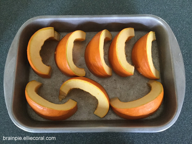 The pumpkin halves have been sliced into eight crescent moon-shaped pieces, sitting in a pan of shallow water.