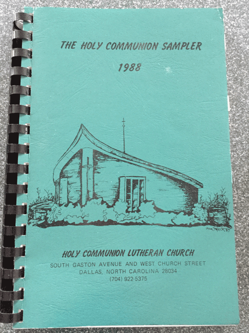 A spiralbound cookbook with a faded green cover. It's titled The Holy Communion Sampler 1988. An ink drawing of a church, with a roof that looks vaguely like a teardrop from an upward view, graces the cover. Below is the text: Holy Communion Lutheran Church, South Gaston Avenue and West Church Street, Dallas, North Carolina 28034, (704) 922-5375.