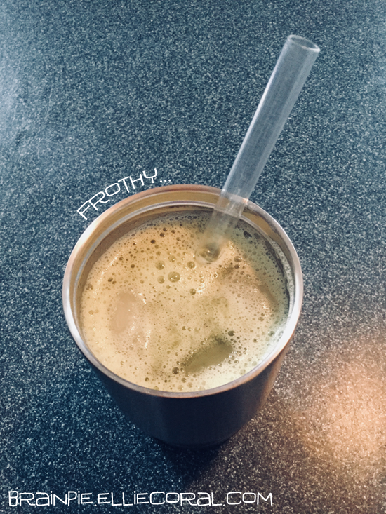 A metal tumbler with a straw containing green, frothy liquid.