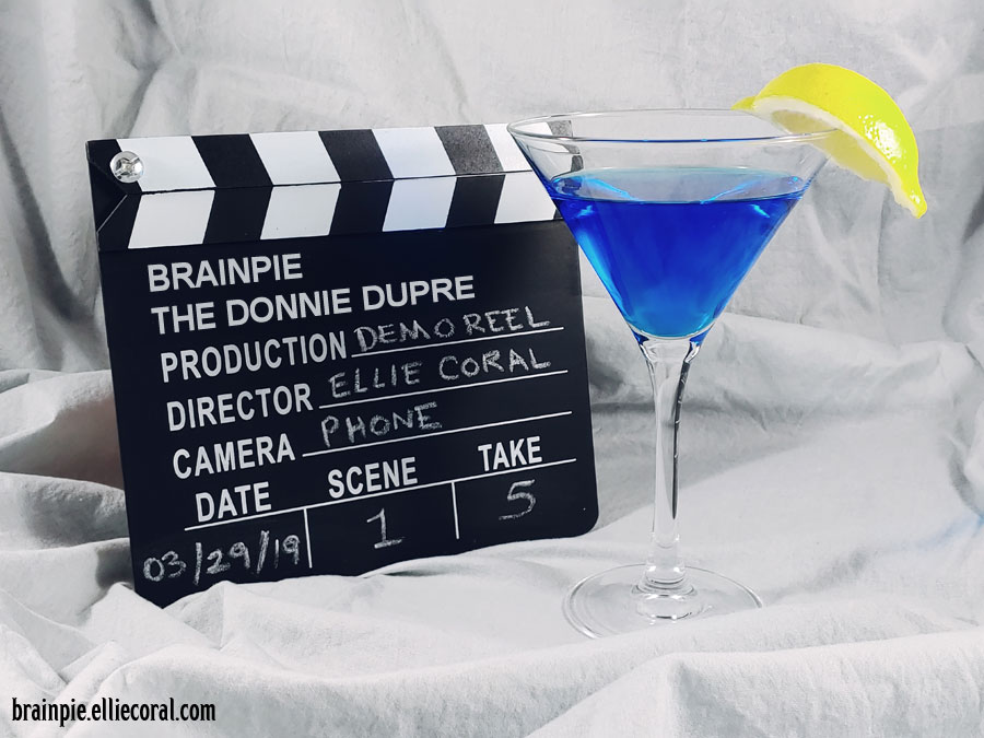 The Brainpie clapperboard reads: The Donnie Dupre, Production: Demo Reel, Director: Ellie Coral, Camera: Phone, Date: 3/29/19, Scene 1, Take 5. The drink is in a martini glass. It's a sapphire blue with a lemon wedge on the rim.